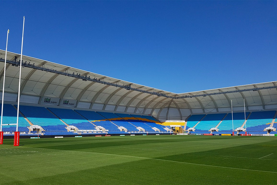 Cbus Super Stadium empty on a clear day, seen from the field between the goalposts, its blue seating under a white curved roof