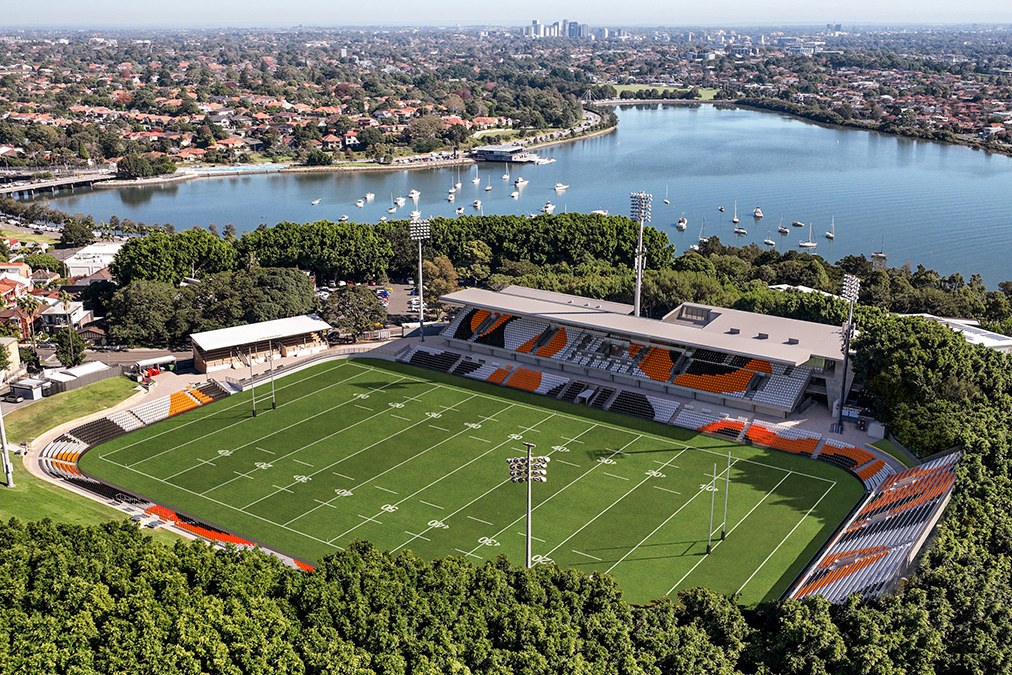Leichhardt Oval from the air, the ground ringed by trees and suburban streets with a boat-filled bay behind it