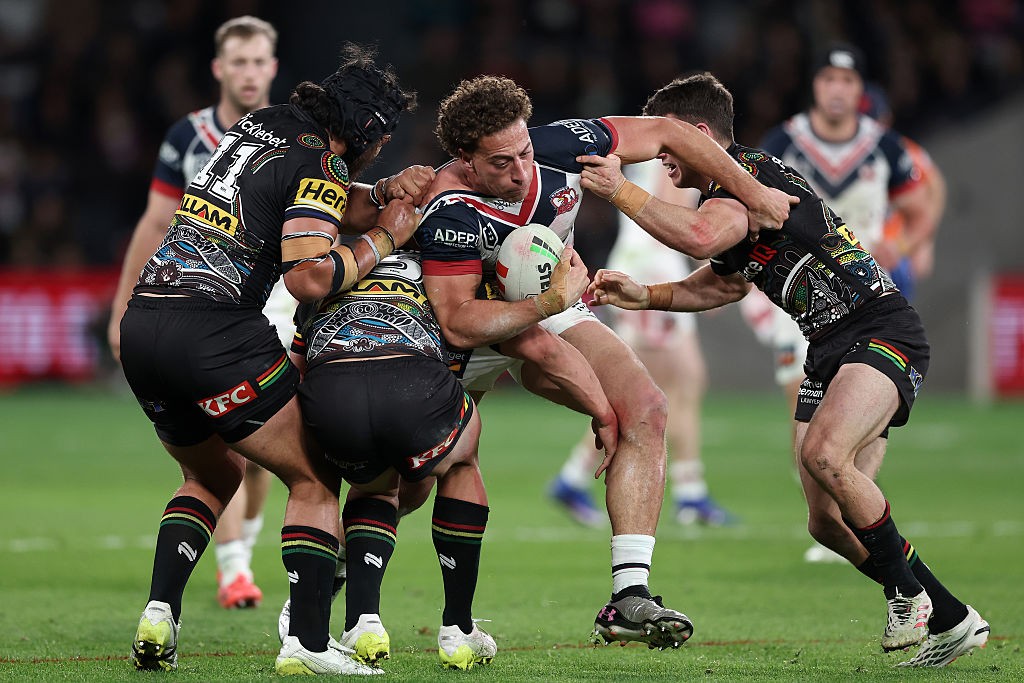 Three Penrith defenders in Indigenous-round jerseys wrap up a Roosters player carrying the ball