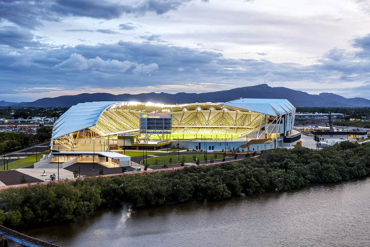 Queensland Country Bank Stadium seen from outside in daylight, sitting on the riverbank with hills rising behind Townsville