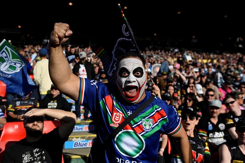 A New Zealand Warriors supporter in black-and-white face paint cheers from a packed grandstand